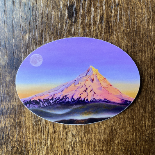 Oval sticker with a mountain Mt Hood and full moon design and colorful violet orange sky on a wooden surface