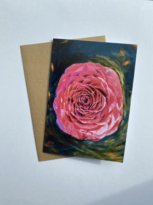Greeting card featuring a painting of a magenta and pink Persian buttercup flower that is blooming. The background is an expressionist green, yellow and orange, and brown envelope on a light gray background